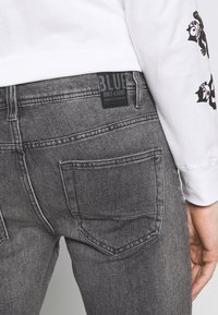 Jeans de denim cinza com um aspeto ligeiramente desbotado, apresentando dois bolsos traseiros e um rótulo preto com a inscrição "BLUE ONLY & SONS" na cintura.
