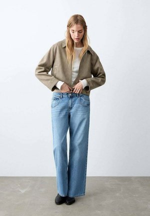 Chaqueta corta caqui con cuello, camiseta blanca de canalé debajo y vaqueros de pierna ancha azul claro. Botines negros completan el conjunto.