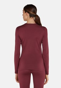 Camicia bordeaux a maniche lunghe in tessuto texturizzato, con dettagli delle cuciture e un fit rilassato, abbinata a pantaloni aderenti coordinati.