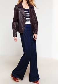 Burgundy lädermotorcykeljacka med dragkedja, kombinerad med en randig blå och vit topp samt marinblå vida byxor. Röda klacksandaler.