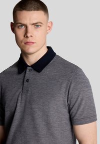 Grijze polo met een marineblauwe kraag, korte mouwen, een placket met twee knopen en een textuurstof, met een getailleerd ontwerp en strakke lijnen.