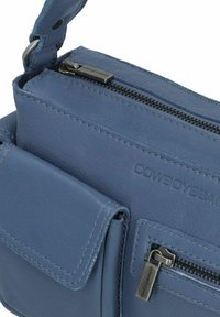 Borsa a spalla in pelle blu con molteplici scomparti con zip, superficie texturizzata e dettaglio del logo. Presenta una tasca frontale con patta e una tracolla robusta.