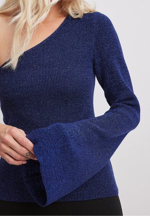 Blauw geribd gebreid topje met één blote schouder en lange uitlopende mouw, gedragen door een persoon met een lichte handtattoo en blond haar.