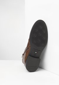 Stivale alla caviglia in pelle marrone con dettaglio sulla cerniera e suola in gomma nera testurizzata con motivi a rotondo e logo del marchio impresso.