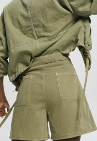 Oliivivihreät, kevyet puuvillasekoitehousut korkean vyötärön kanssa, joissa on kaksi takataskua ja nyörityksellä varustettu vyötärö.