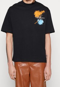 Black cotton t-shirt featuring vibrant orange and blue abstract graphic; relaxed fit with short sleeves and crew neck design.