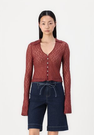 Burgunderfarget bluse med lange ermer i blonder, med dyp V-hals, knappestolpe og strukturert mønster, kombinert med mørk denimshorts med snøring.