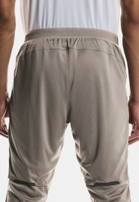 Pantaloni sportivi grigi con una texture liscia, vita elastica e design affusolato. Presentano dettagli neri vicino all'orlo.
