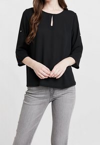 Musta pusero, jossa on avonainen pääntie, kolmen neljänneksen hihat ja koristeelliset nappikoristeet hihoissa, valmistettu sileästä kankaasta.