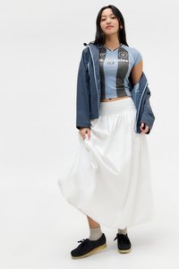 Top sportivo accorciato blu e grigio con stampa grafica, abbinato a una gonna maxi bianca e fluida e scarpe nere con calzini chiari.