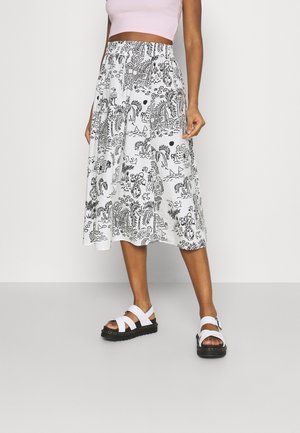 Jupe midi blanche avec imprimé noir à thème nature, dotée d'une taille élastique et d'une coupe fluide. Associée à des sandales blanches avec semelle noire.