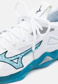 Scarpa da ginnastica bianca con accenti turchesi, tomaia in rete testurizzata, lacci e un elemento di design ondulato sul lato. Presenta il marchio Mizuno.