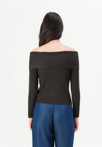 Dark brown ribbed off-the-shoulder sweater with long sleeves, fitted design, and a wide neckline, paired with blue wide-leg jeans.