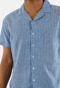 Lichtblauw overhemd met korte mouwen, witte verticale strepen, knoopsluiting aan de voorkant en een spread collar. Gemaakt van textuurstof.