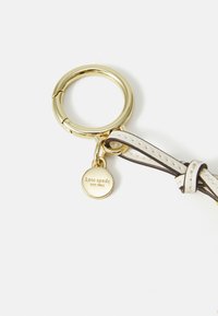 Gold keyring attached to a white leather strap with a small round charm engraved "kate spade new york."