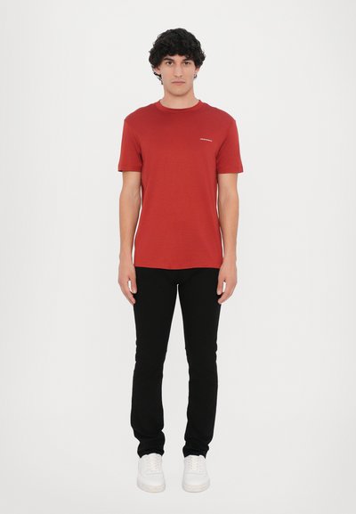 Rotes kurzärmliges T-Shirt aus weichem Stoff, kombiniert mit schwarzen Slim-Fit-Jeans und weißen Sneakers. Einfaches Design mit Rundhalsausschnitt.