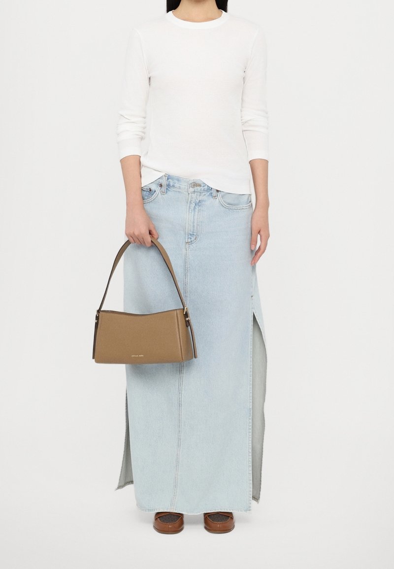 Sac à main marron au design structuré avec une poignée courte, porté avec une chemise blanche à manches longues et une jupe longue en denim bleu clair avec des fentes latérales.