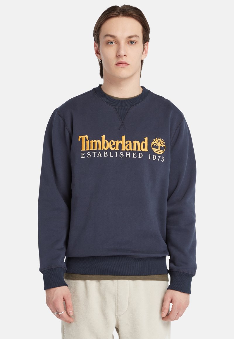 Navyblauwe sweatshirt met ribbelboorden en onderkant. Kenmerkt het "Timberland ESTABLISHED 1973" logo in gele borduursel aan de voorkant. Zachte textuur.