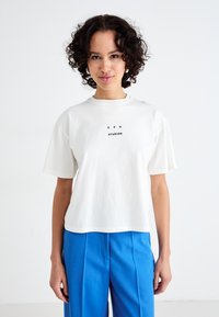 Hvid bomulds T-shirt med korte ærmer, prydet med en centreret sort tekstprint "C P H STUDIOS." Sammen med blå skræddersyede bukser.