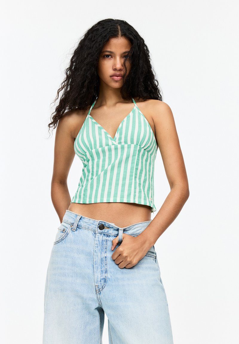 Groen en wit gestreept haltertop met een V-hals ontwerp, cropped lengte en een lichte textuur. Gecombineerd met lichtblauwe high-waisted jeans.