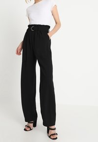 Pantalons larges noirs à taille haute, avec un détail de ceinture volé et une boucle en argent, associés à un haut blanc à manches courtes en maille côtelée.