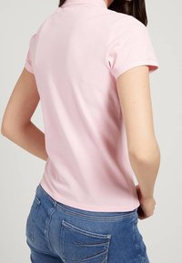 Camisa polo rosa de manga corta, hecha de una tela suave y ligera. Presenta un collar doblado y un dobladillo recto.