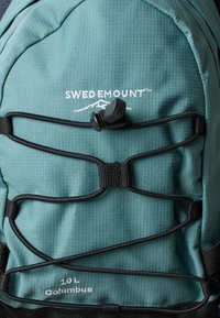 Turkizno moder nahrbtnik Swedemount Columbus 10L z črnimi elastičnimi vrvicami in nastavljivim zadrževalcem na sprednji plošči.