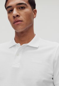 Vit polo skjorta med texturerad tyg, med en klassisk krage, plagg med två knappar och en subtil logotyp på bröstet.