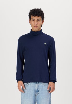 Chandail turtleneck à manches longues bleu marine en tissu doux, doté d'un petit logo brodé vert sur la poitrine et d'une coupe décontractée.