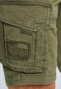 Grüne Cargo-Shorts aus Baumwolle, mit einem strukturierten Patch mit eingeprägtem Text, seitlichen Taschen und einem robusten Stoffdesign.