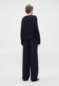 Ναυτική πλεκτή μπλούζα με ραβδωτή υφή, διαθέτοντας στρογγυλή λαιμόκοψη και ρίγες στους ώμους, συνδυασμένη με παντελόνι φαρδύ με ρίγες.