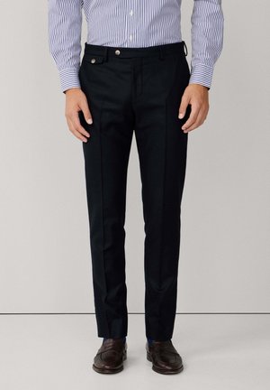 Marineblaue, taillierte Hosen mit glatter Textur, flacher Vorderseite, seitlichen Taschen und silbernen Hardware-Akzenten, kombiniert mit braunen Loafers.