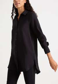 Camicia nera a maniche lunghe con colletto abbottonato, caratterizzata da un tessuto testurizzato, una vestibilità ampia e spacco laterale sull'orlo.