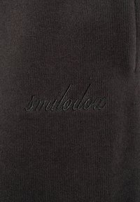 Tessuto nero a coste con la parola "smilodoc" ricamata in filo nero abbinato con lettere in corsivo.