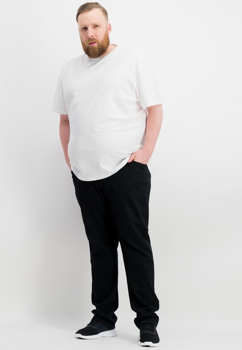 T-shirt bianca in cotone con orlo arrotondato, abbinata a pantaloni neri e sneaker nere. Tessuto morbido, vestibilità comoda, senza motivi visibili.