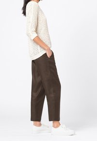 Beige pletený svetr s tříčtvrtečními rukávy, kombinovaný s hnědými volnými kalhotami a bílými teniskami, zobrazený z bočního profilu.