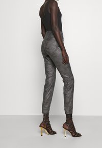 Grå fusk läderbyxor med slim fit, hög midja och subtil textur. Kombineras med bruna sandaler med hög klack och remmar som har guldaccent.