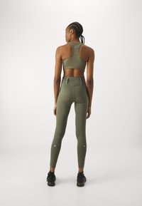 Olivgrüner Sport-BH und hoch taillierte Leggings, ausgestattet mit strukturiertem Stoff und reflektierenden Akzenten, kombiniert mit schwarzen Sportschuhen.