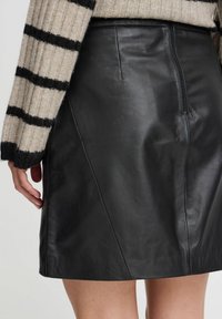 Falda de cuero negra con un diseño ajustado y costuras sutiles. Cierre de cremallera en la parte posterior, combinada con un suéter a rayas en beige y negro.