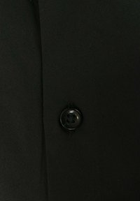 Tela negra con una textura suave, que presenta un botón negro redondo de cuatro agujeros cosido al material.