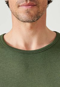 T-shirt in cotone verde scuro con scollo rotondo, caratterizzato da una texture liscia e cuciture ordinate attorno al colletto e alle spalle.