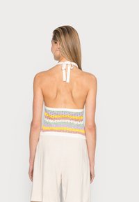 Top de halter de punto con franjas horizontales multicolores en tonos pastel, con un lazo blanco en el cuello y un diseño de espalda abierta.