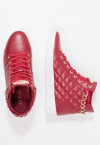 Red high-top sneakers featuring a quilted texture, white rubber sole, gold eyelets, and chain accents on the collar. Brand logo visible inside.