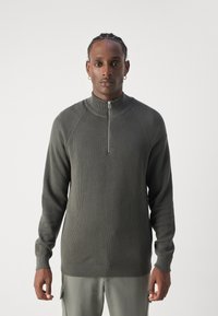 Pulover închis la culoare, din material texturat, cu fermoar, mâneci lungi și guler înalt. Are un fermoar argintiu și un design cu mâneci raglan.