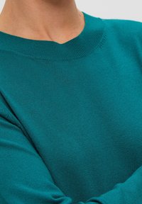 Suéter de punto en color verde azulado con un escote redondo. Presenta una textura suave y ribetes acanalados en el cuello y los puños. Mangas largas.