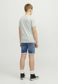 Vaaleanharmaa lyhythihainen t-paita, siniset farkkushortsit käännetyillä lahkeilla, mustat korkeat sneakersit ja valkoiset nilkkasukat, nähtynä takaa.