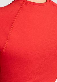 Rode sportshirt van gladde, elastische stof met een ronde hals en platte naden voor comfort. Close-up van de textuur van het materiaal.