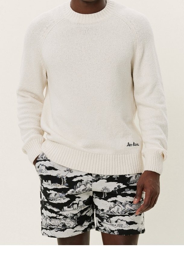 Krämfärgad ribbad stickad tröja med rund halsringning, kombinerad med svartvita mönstrade shorts med ett landskapsmönster.