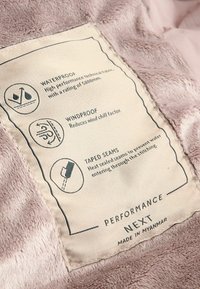 Étiquette de performance sur un tissu doux et léger violet clair. Les détails incluent imperméable, coupe-vent et coutures scellées pour une résistance à l'eau. Bords finement découpés.