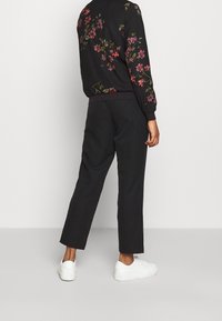 Blouson aviateur noir à fleurs avec broderies roses et vertes. Associé à un pantalon noir fuselé et des baskets blanches.